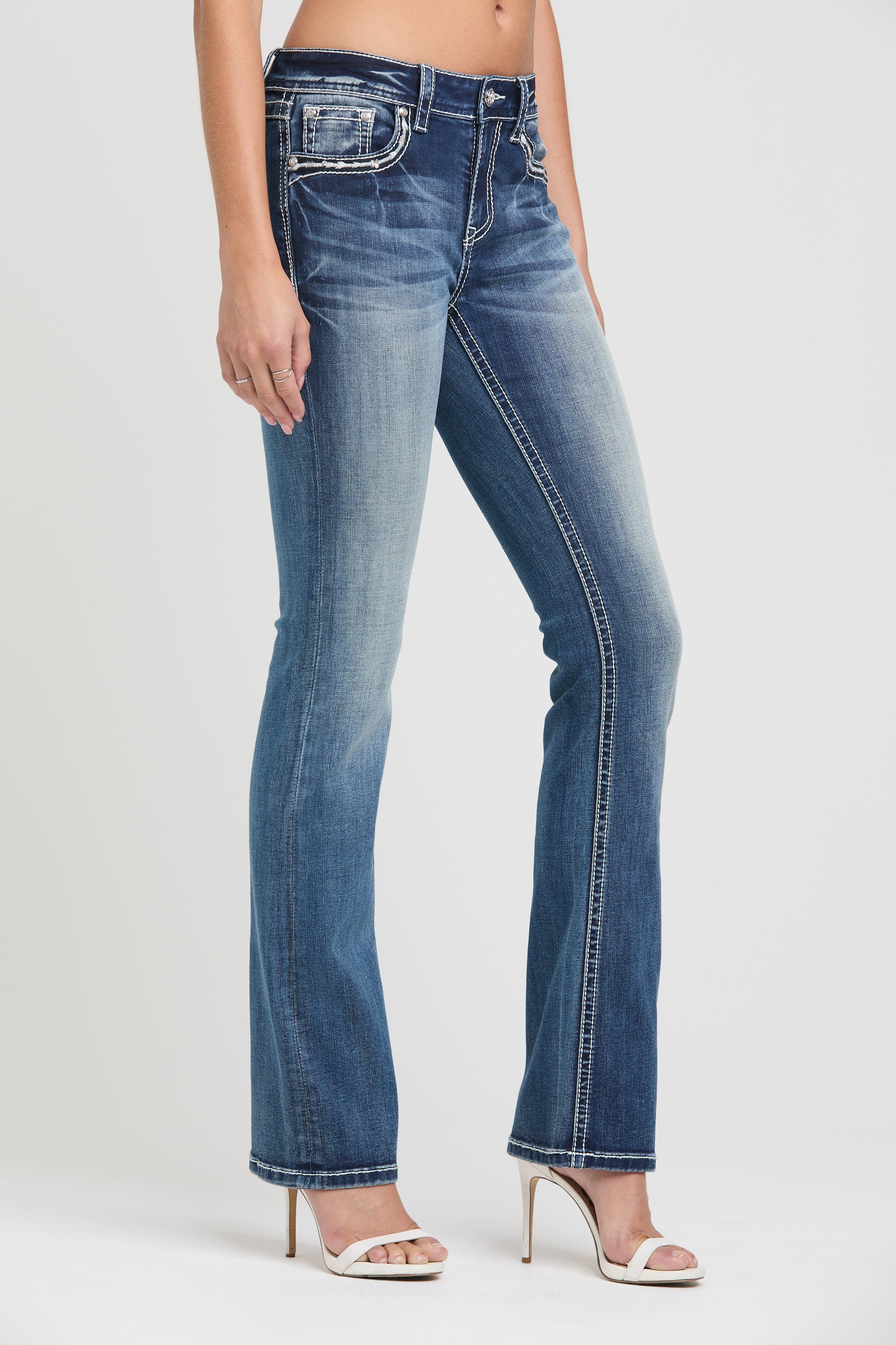 Grace in LA womens bootcut jeans in a dark featuring a slim fit silhouette, white contrast stitching on the side seams, and styled with white heels.