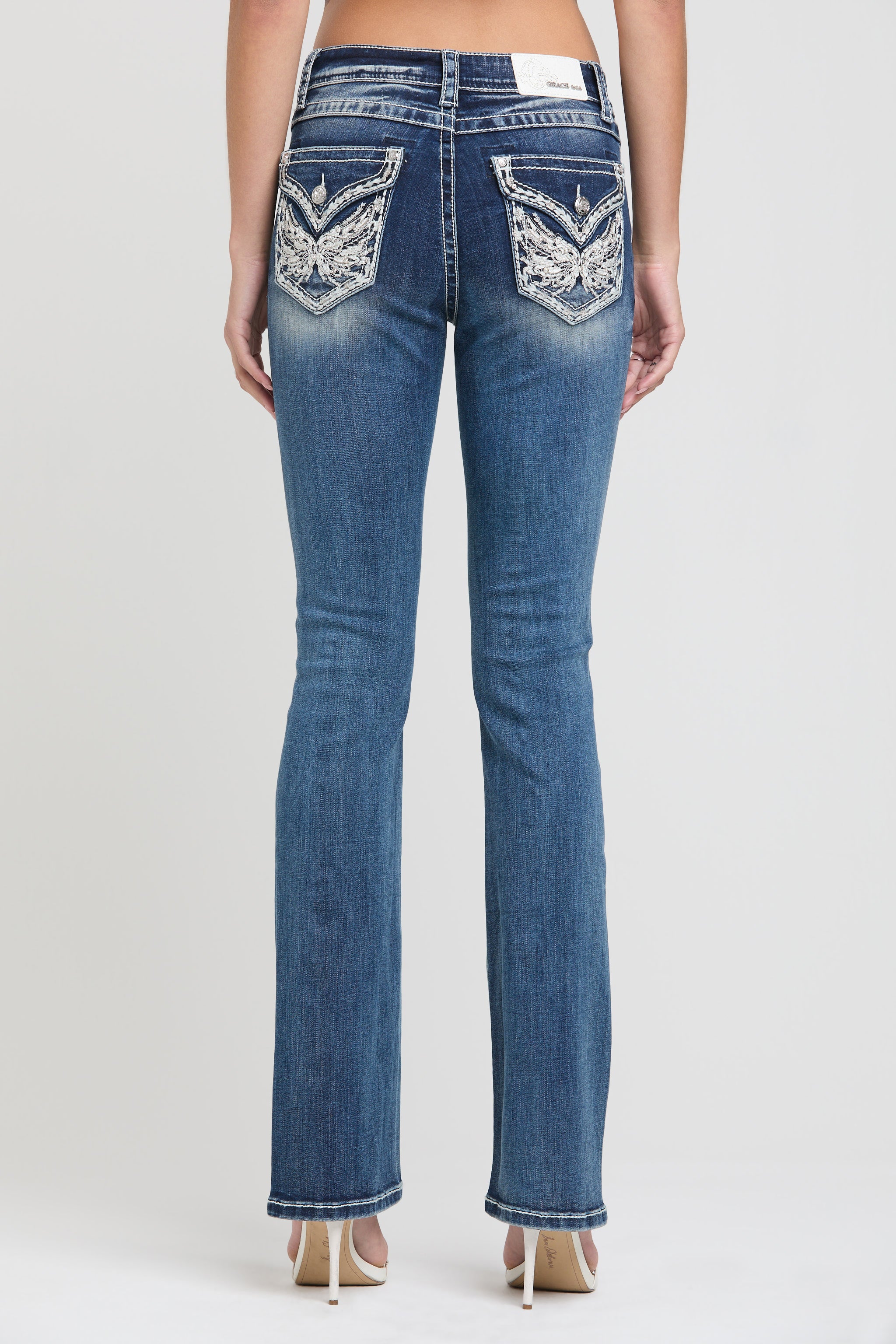 Grace in LA womens bootcut jeans in a dark featuring a full rear view with symmetrical white and silver floral wing embroidery on both back pockets.