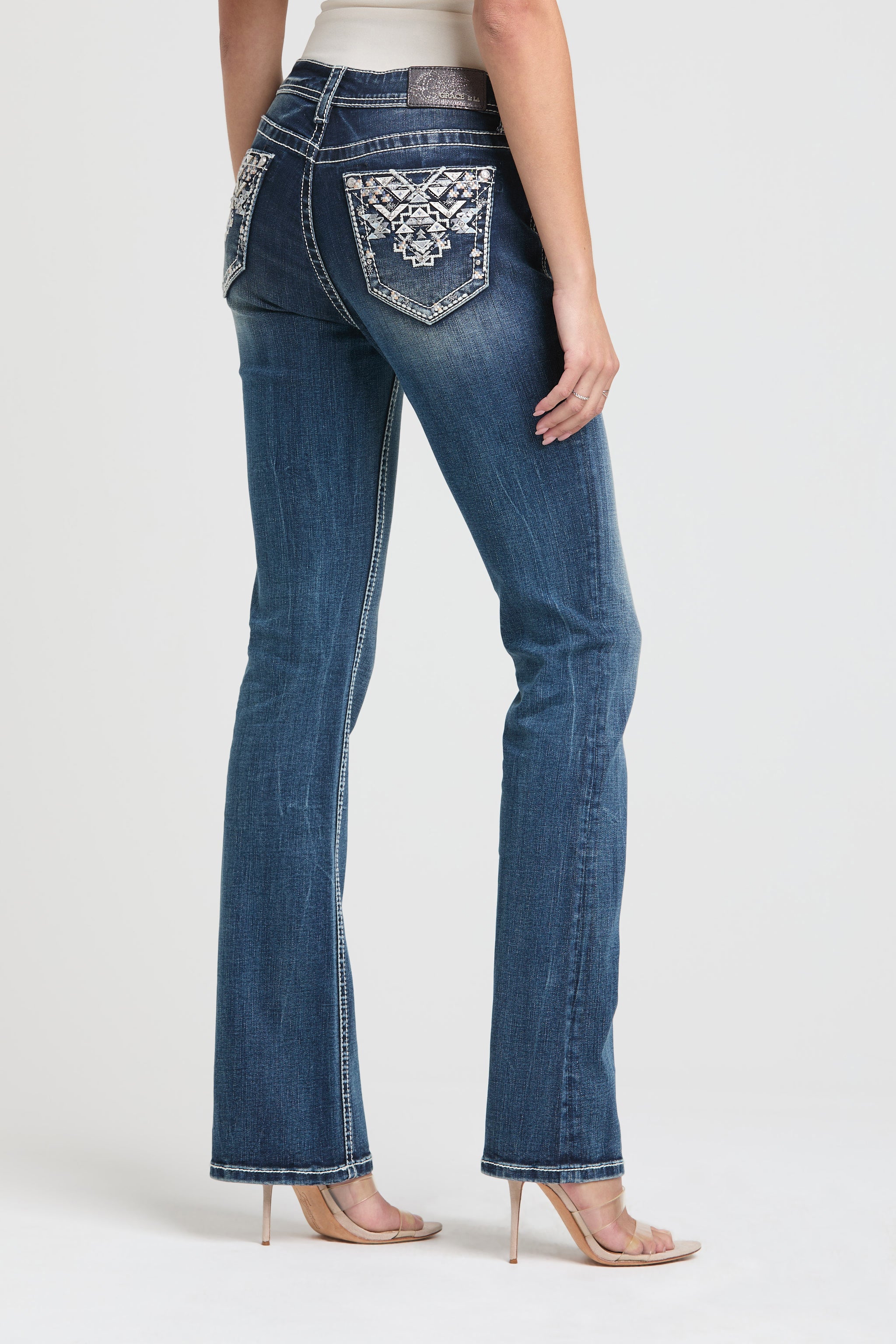 Grace in LA womens bootcut jeans in a dark wash featuring a full rear-view silhouette with symmetrical silver and white Aztec geometric pocket embroidery.
