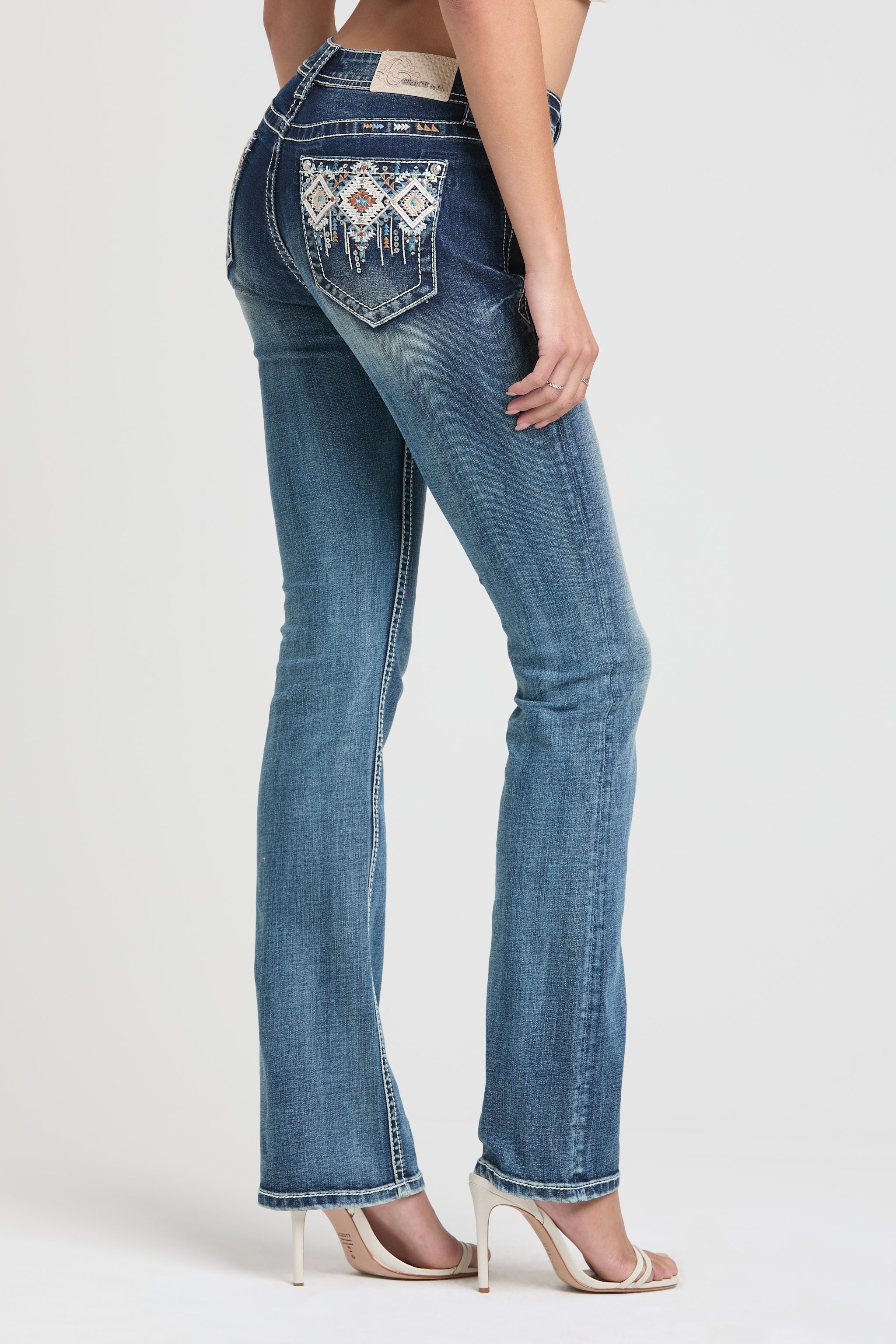 Grace in LA rhinestone jeans for women featuring silver and white crystal-embellished feather embroidery on the front pocket.
