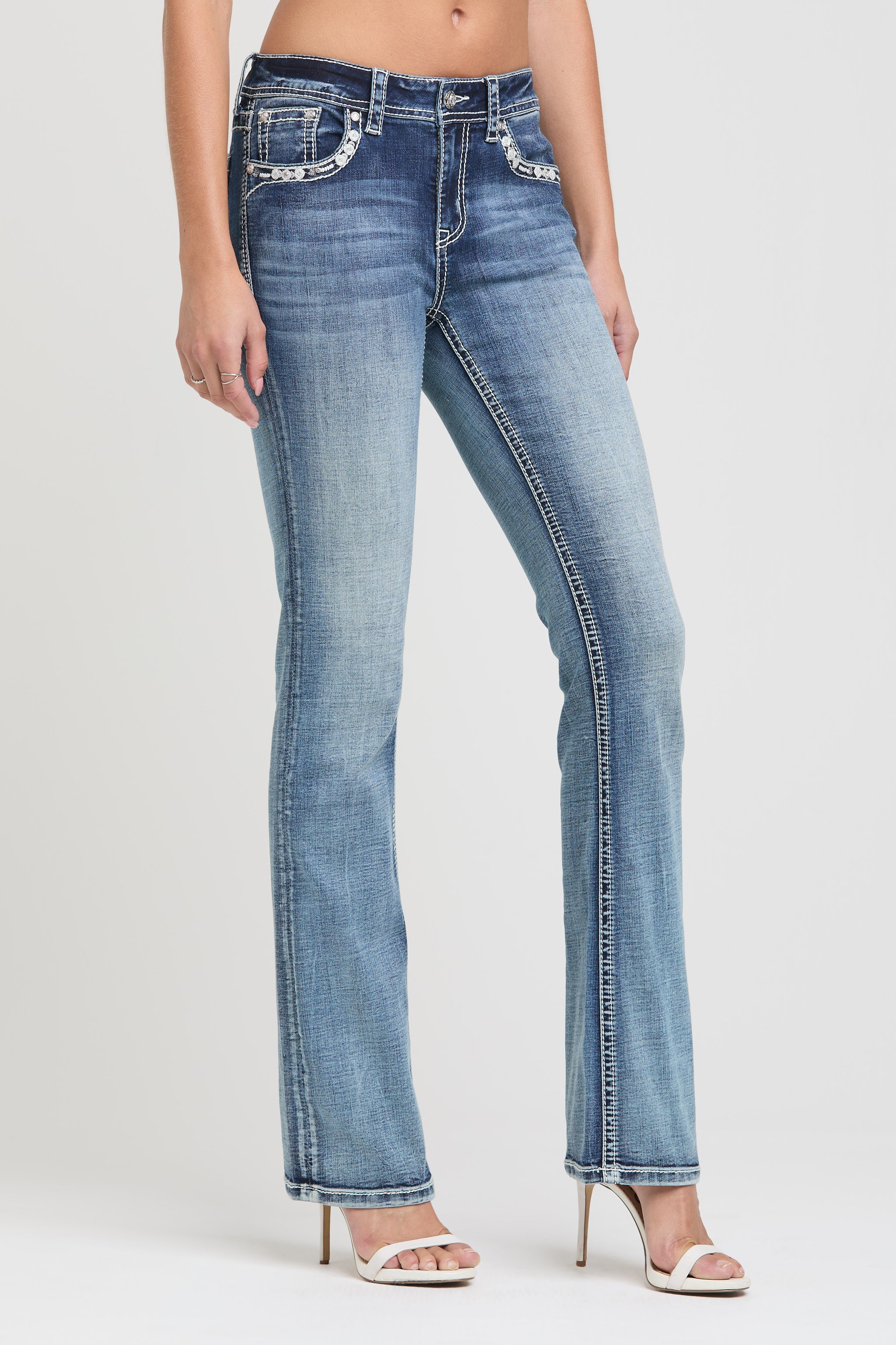 Grace in LA womens bootcut jeans in a medium featuring a side-angle view with silver horseshoe and white floral embroidery on the back pocket.