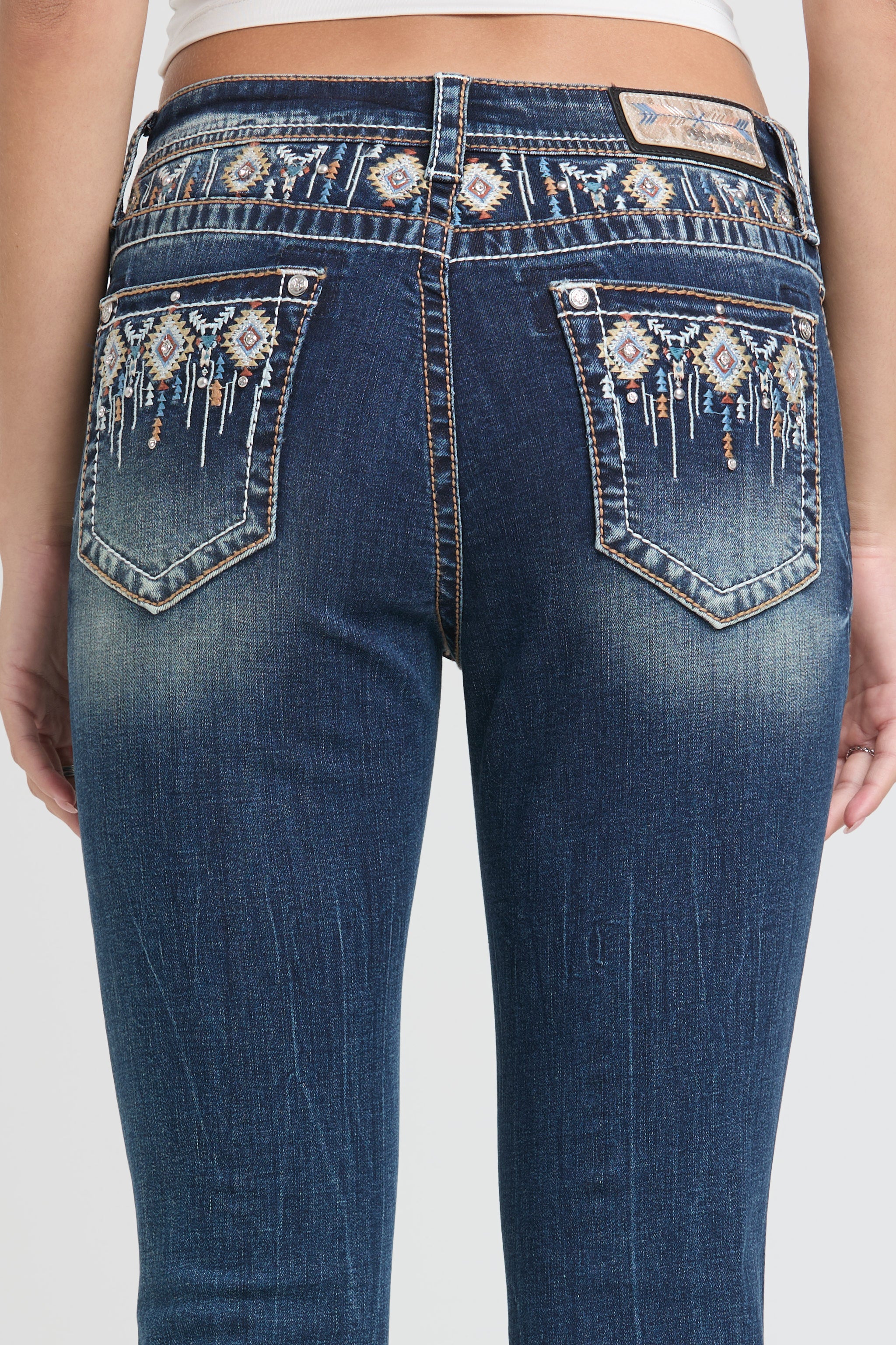 Grace in LA womens bootcut jeans in a dark featuring western-inspired native geometric embroidery and intricate rhinestone detailing on the waistband and back pockets.