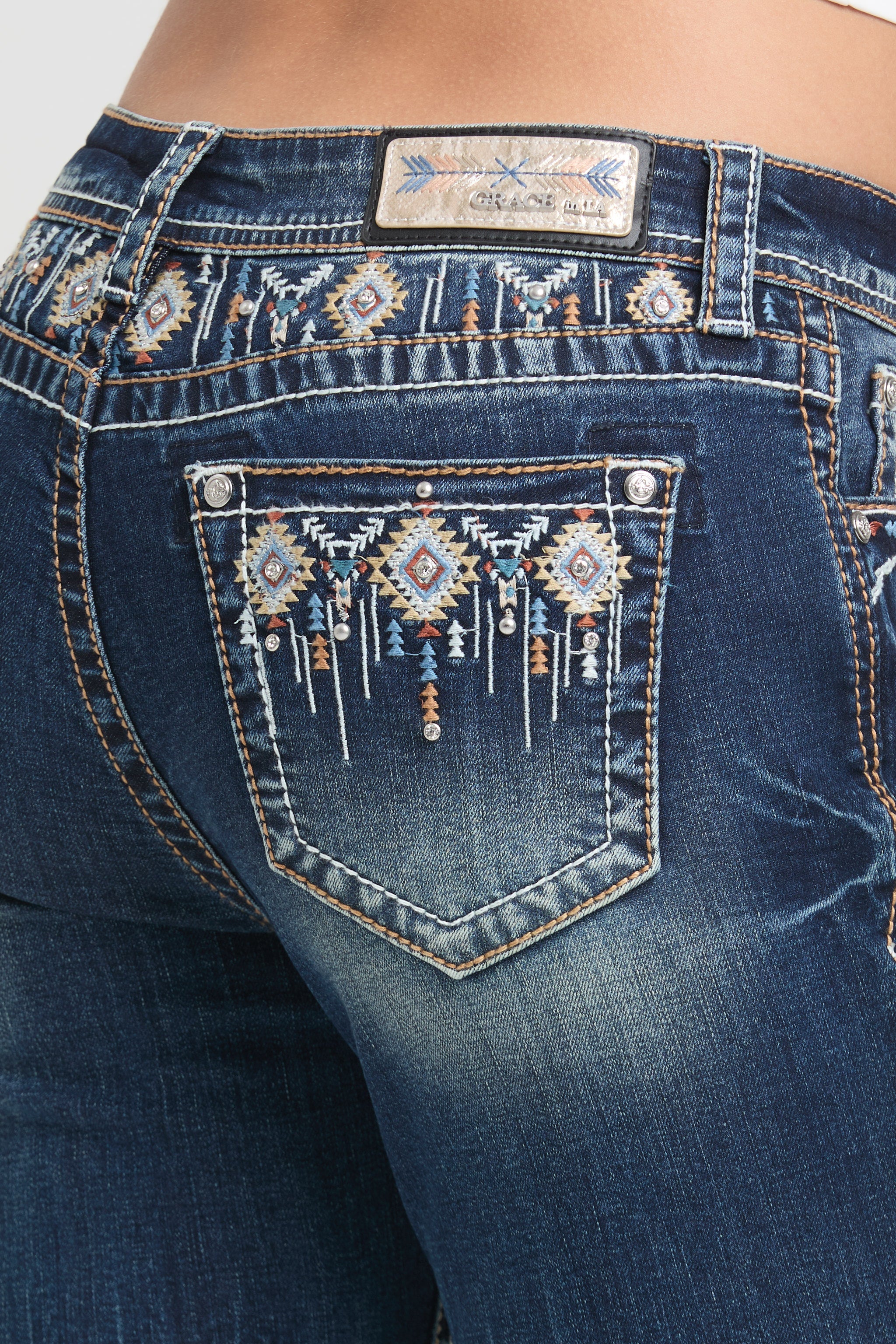 Grace in LA rhinestone jeans for women featuring a dark wash with colorful geometric tribal embroidery and crystal accents on the back pocket.