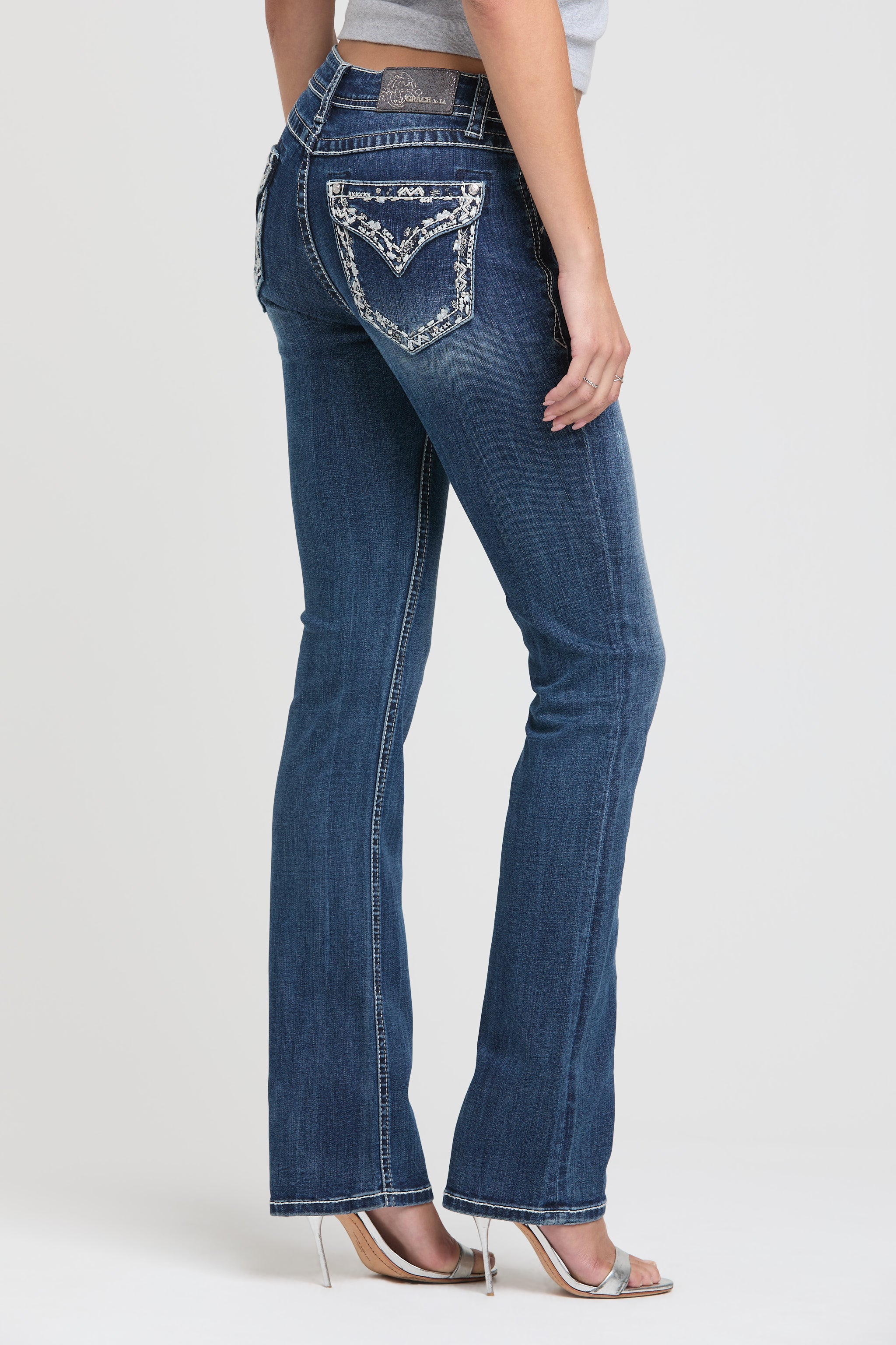 Womens bootcut jeans Full-length angled back view of Grace in LA featuring white floral embroidery and silver studs.