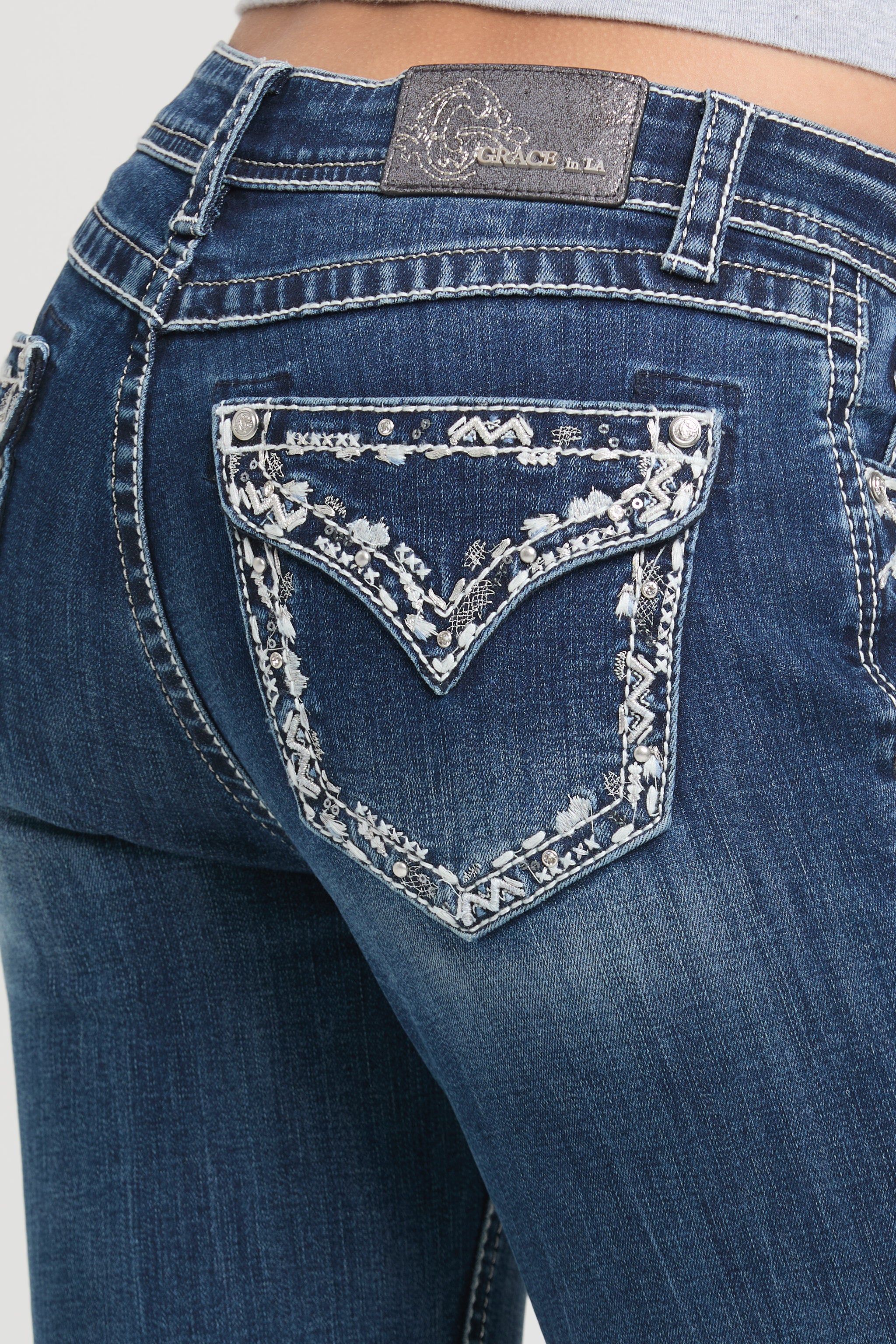 Womens bootcut jeans Close-up of a back pocket featuring intricate white floral embroidery and silver studs on Grace in LA.