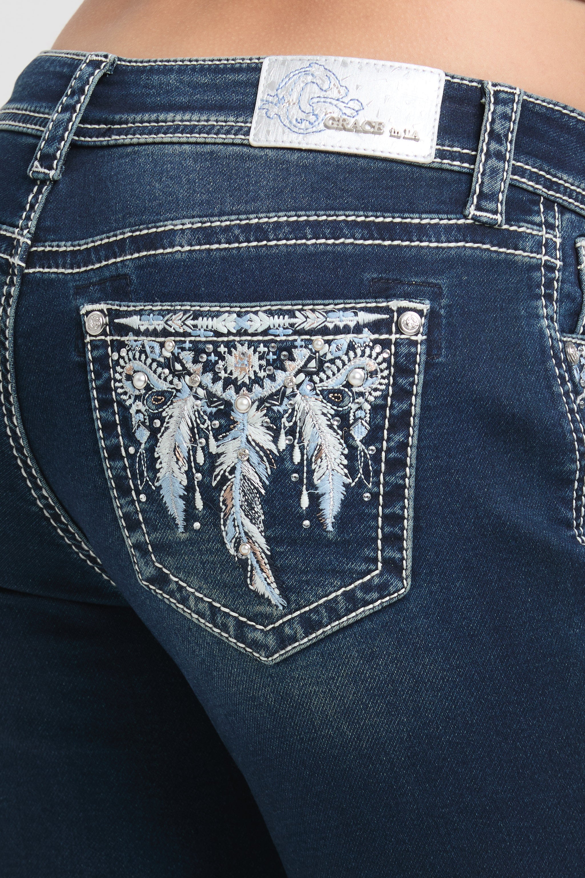Grace in LA womens bootcut jeans in a deep indigo denim finish featuring intricate silver and white bohemian feather embroidery on the back pockets.