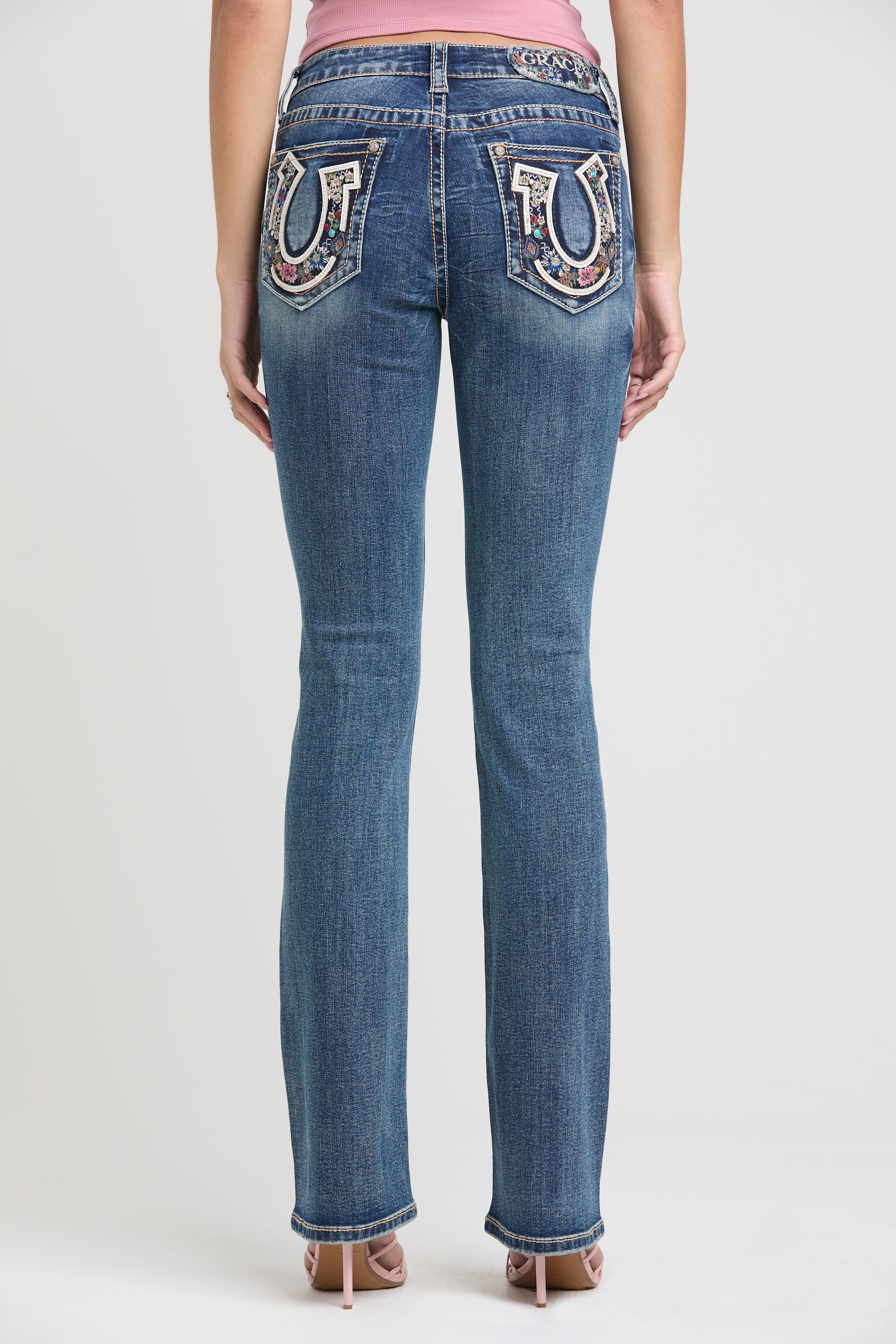 Grace in LA womens bootcut jeans in a medium featuring a full rear view with symmetrical silver horseshoe and multi-color floral embroidery on both back pockets.