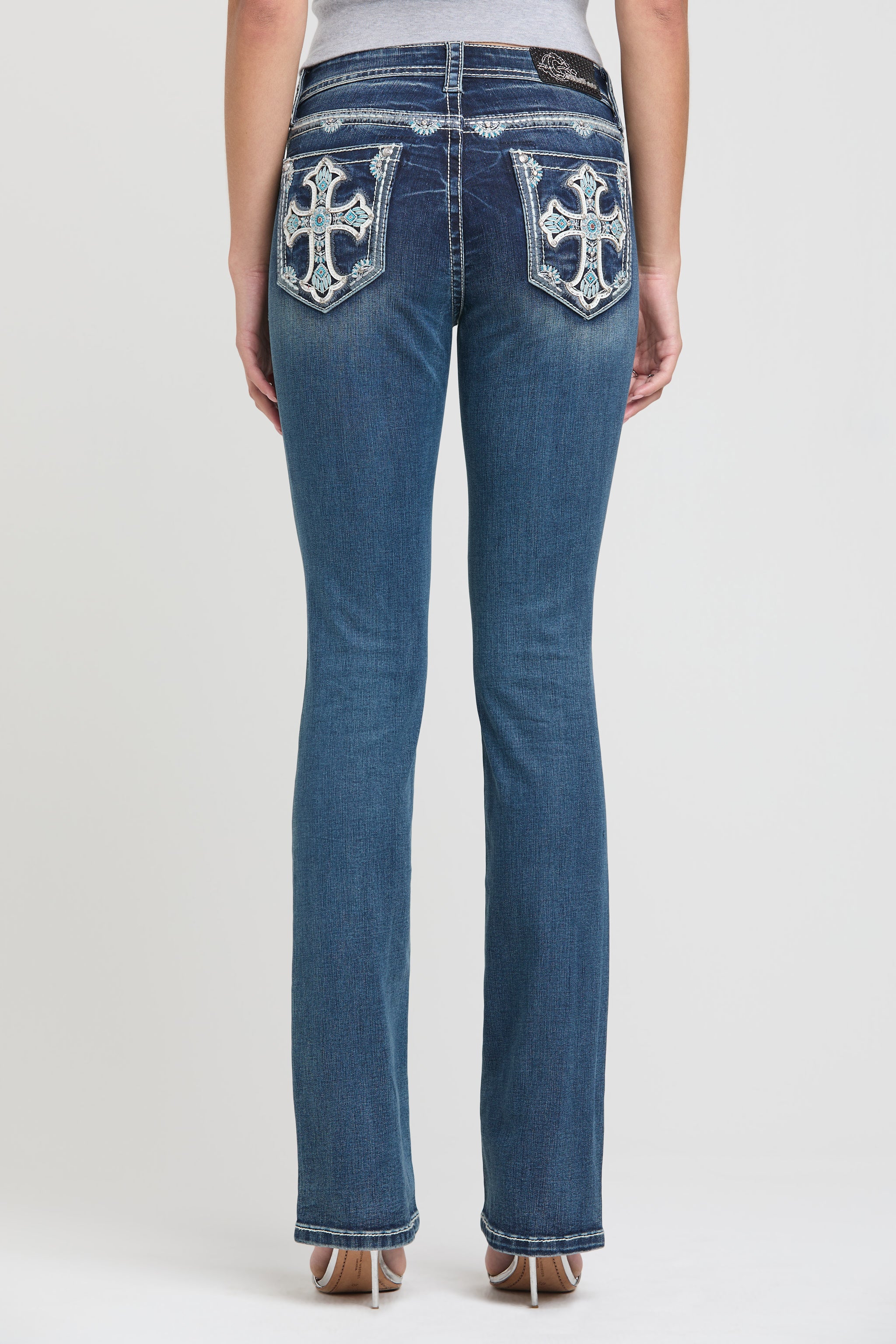 Grace in LA womens bootcut jeans in a dark wash featuring symmetrical white embroidered crosses with turquoise crystal accents on both back pockets.