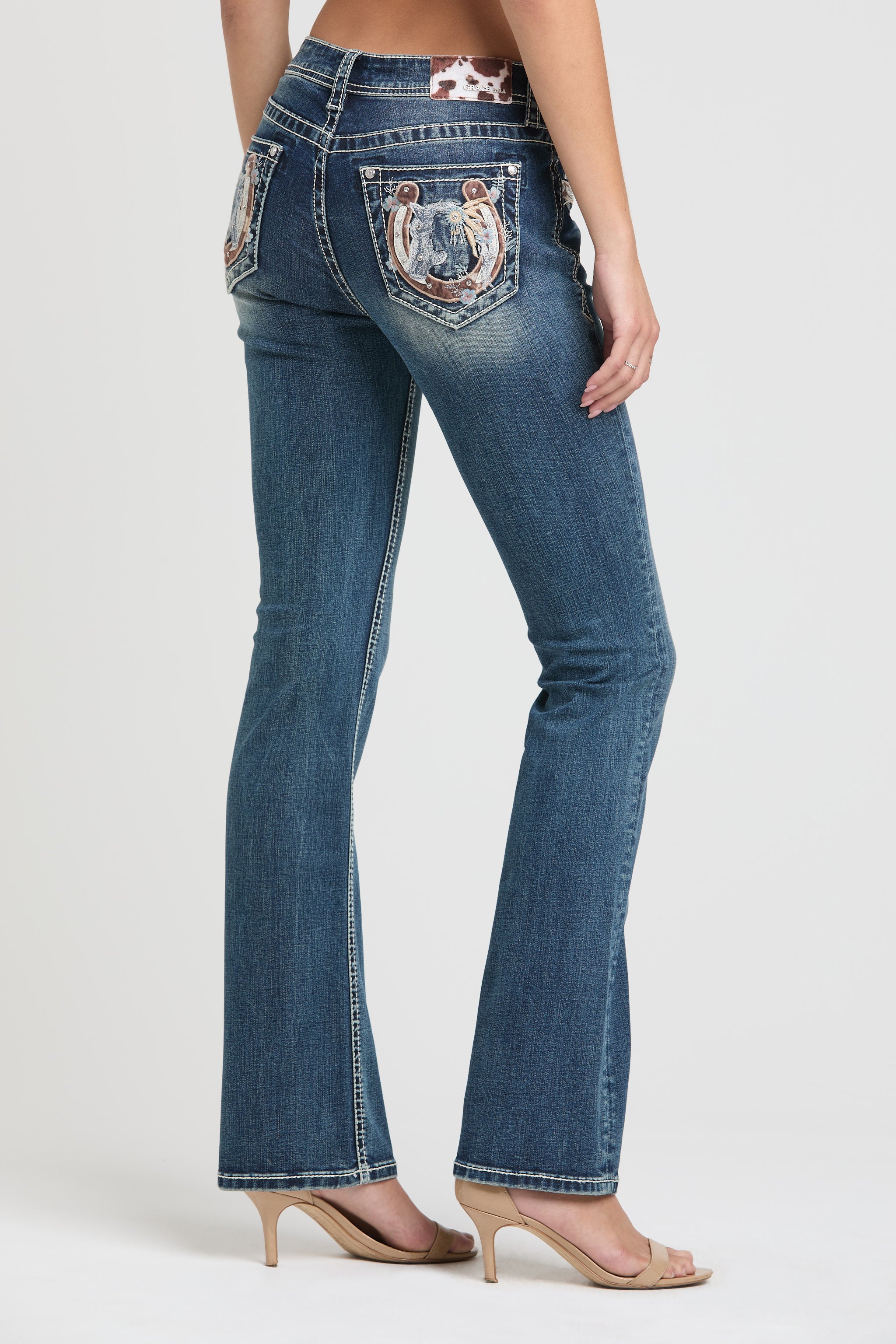 Grace in LA womens bootcut jeans featuring a full-length rear view of an embroidered horseshoe, desert landscape scene, and floral accents on the back pocket.