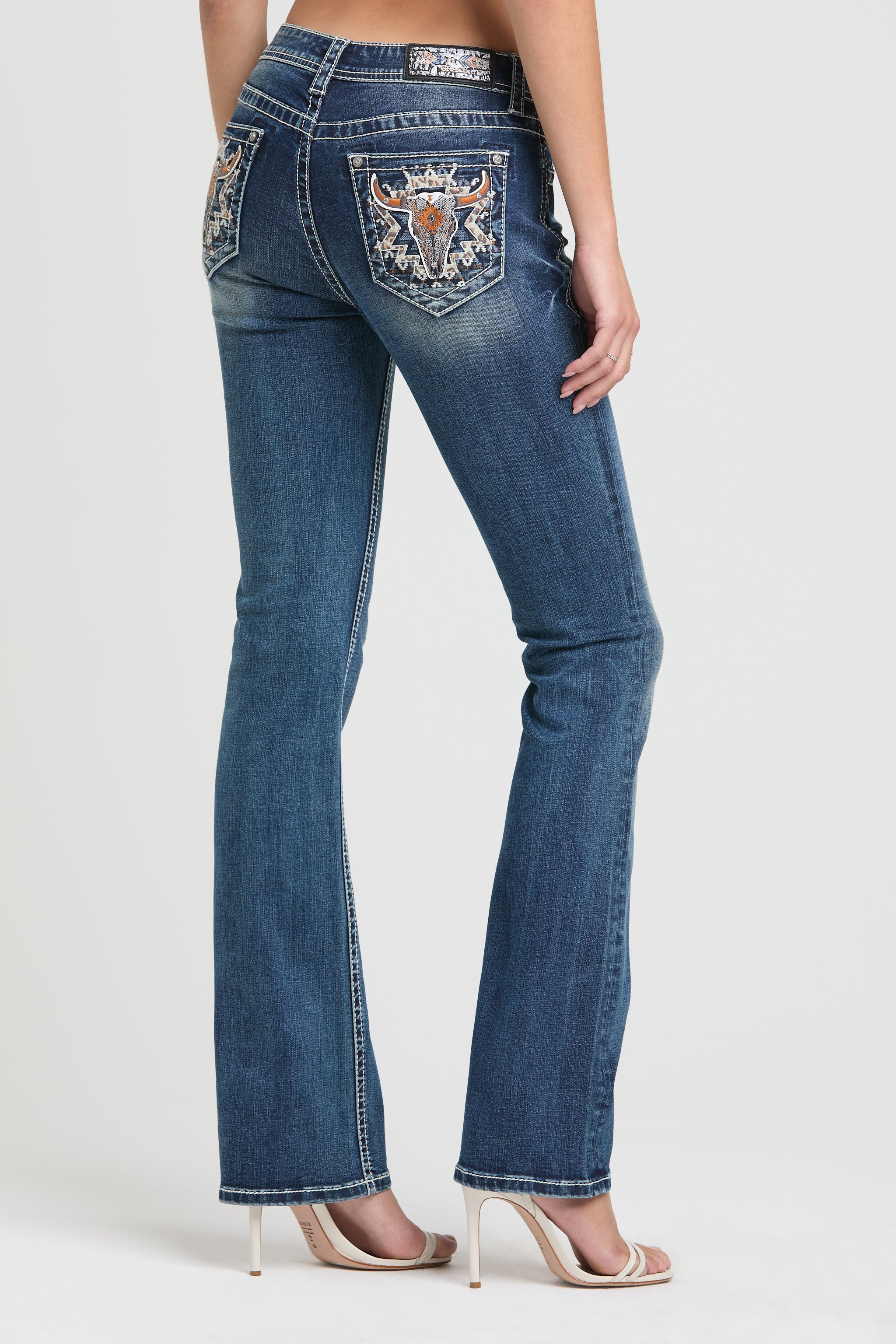 Grace in LA embroidered jeans women featuring a western longhorn bull skull motif with copper horns and an intricate geometric tribal sunburst on the back pocket.