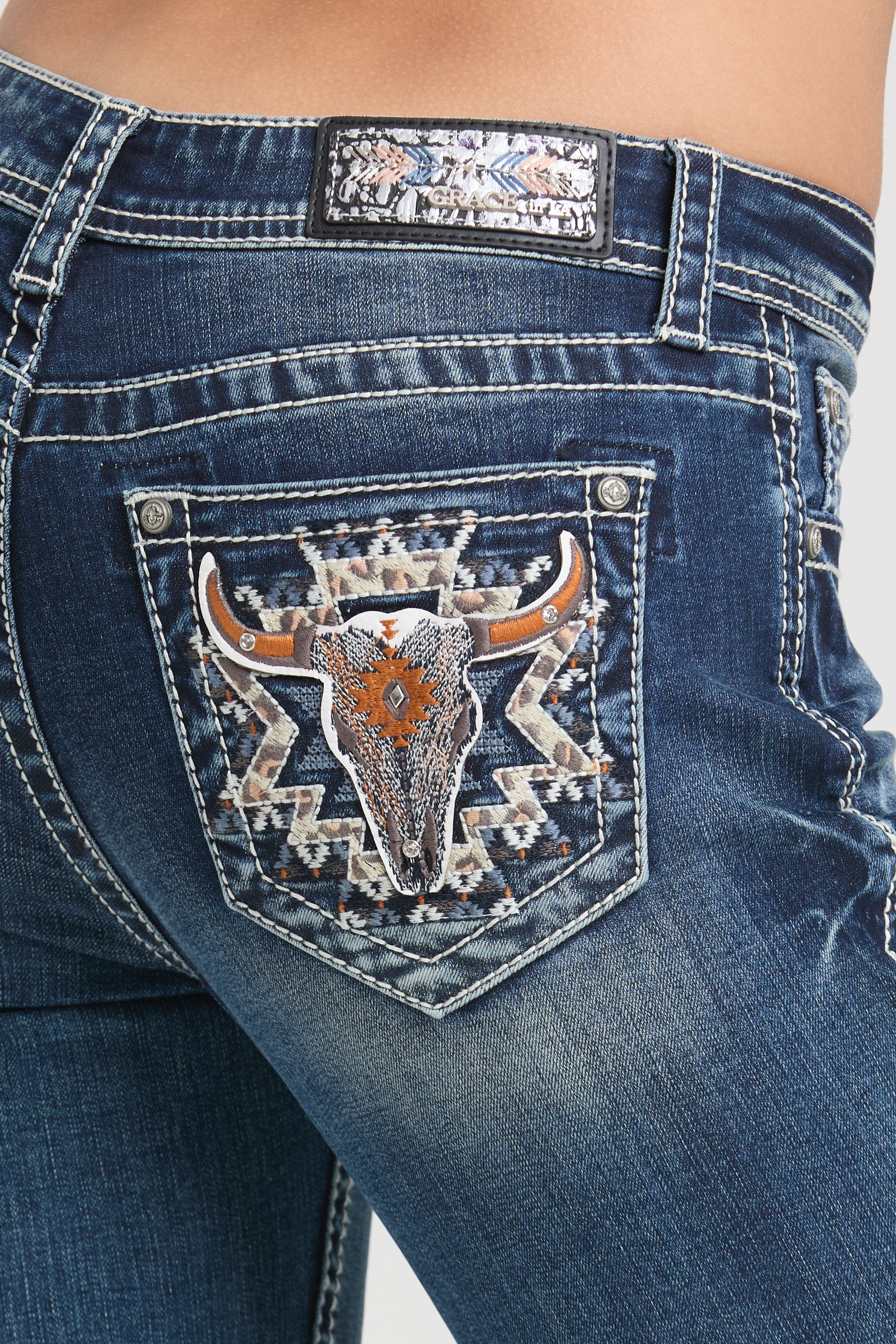Grace in LA embroidered jeans women featuring a western longhorn bull skull motif with copper-colored horns and a tribal geometric star on the back pocket.