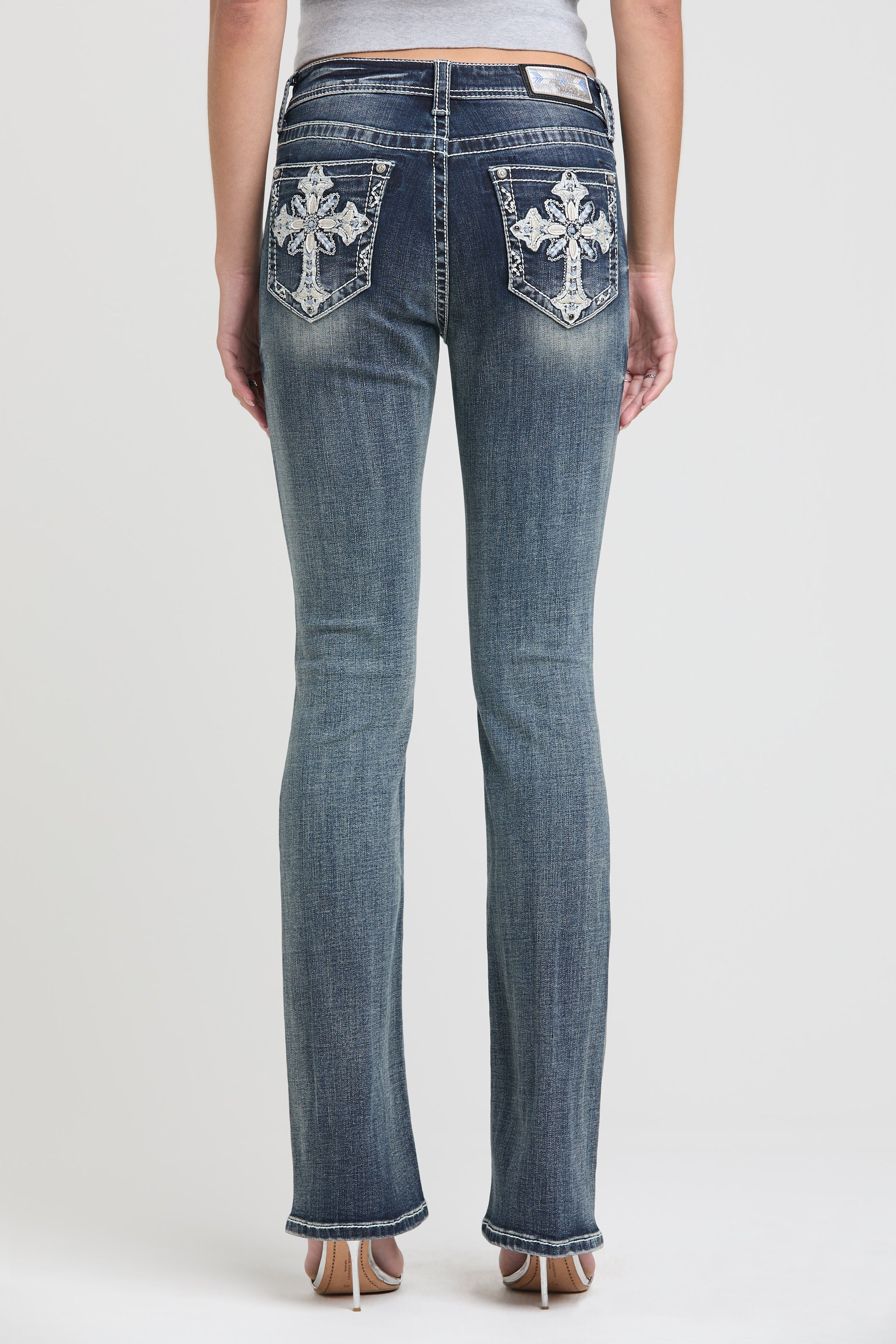 Grace in LA womens bootcut jeans in a medium featuring a full rear view with symmetrical crystal-embellished cross embroidery on both back pockets.