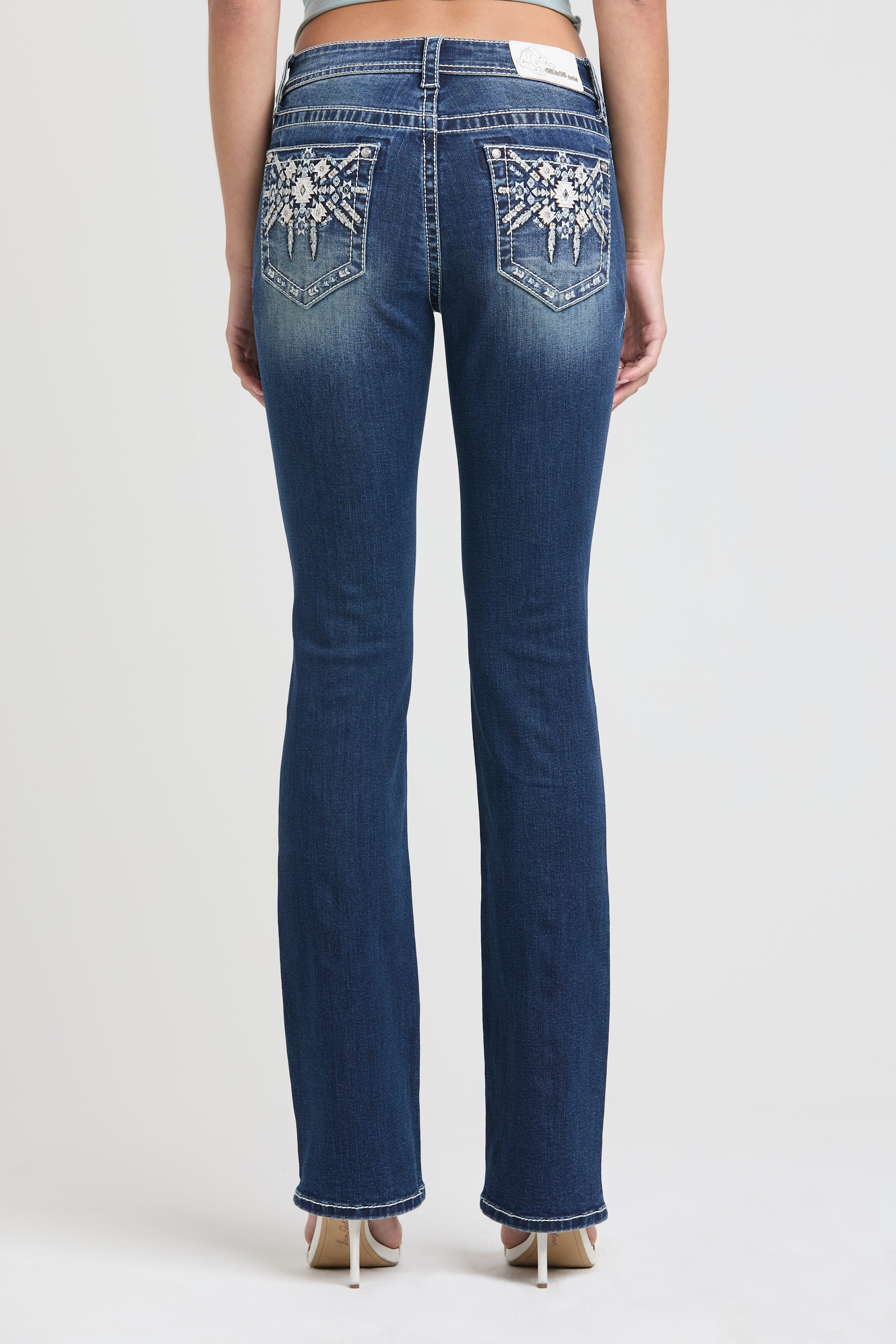 Grace in LA womens bootcut jeans in a dark wash featuring symmetrical white and light blue Aztec geometric embroidery and silver studs on both back pockets.