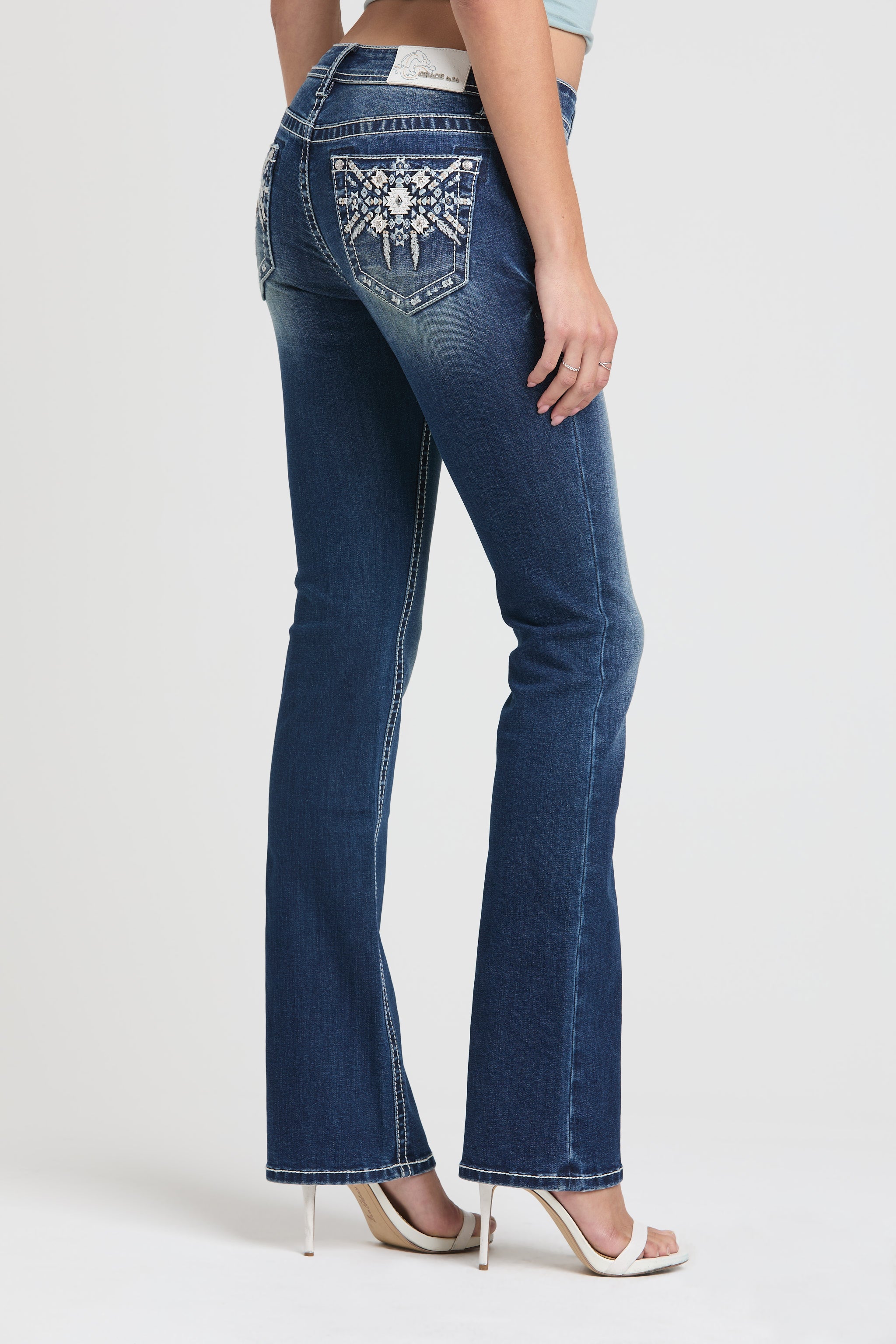 Grace in LA womens bootcut jeans in a dark wash featuring intricate white and light blue Aztec geometric embroidery with silver studs on the back pockets.