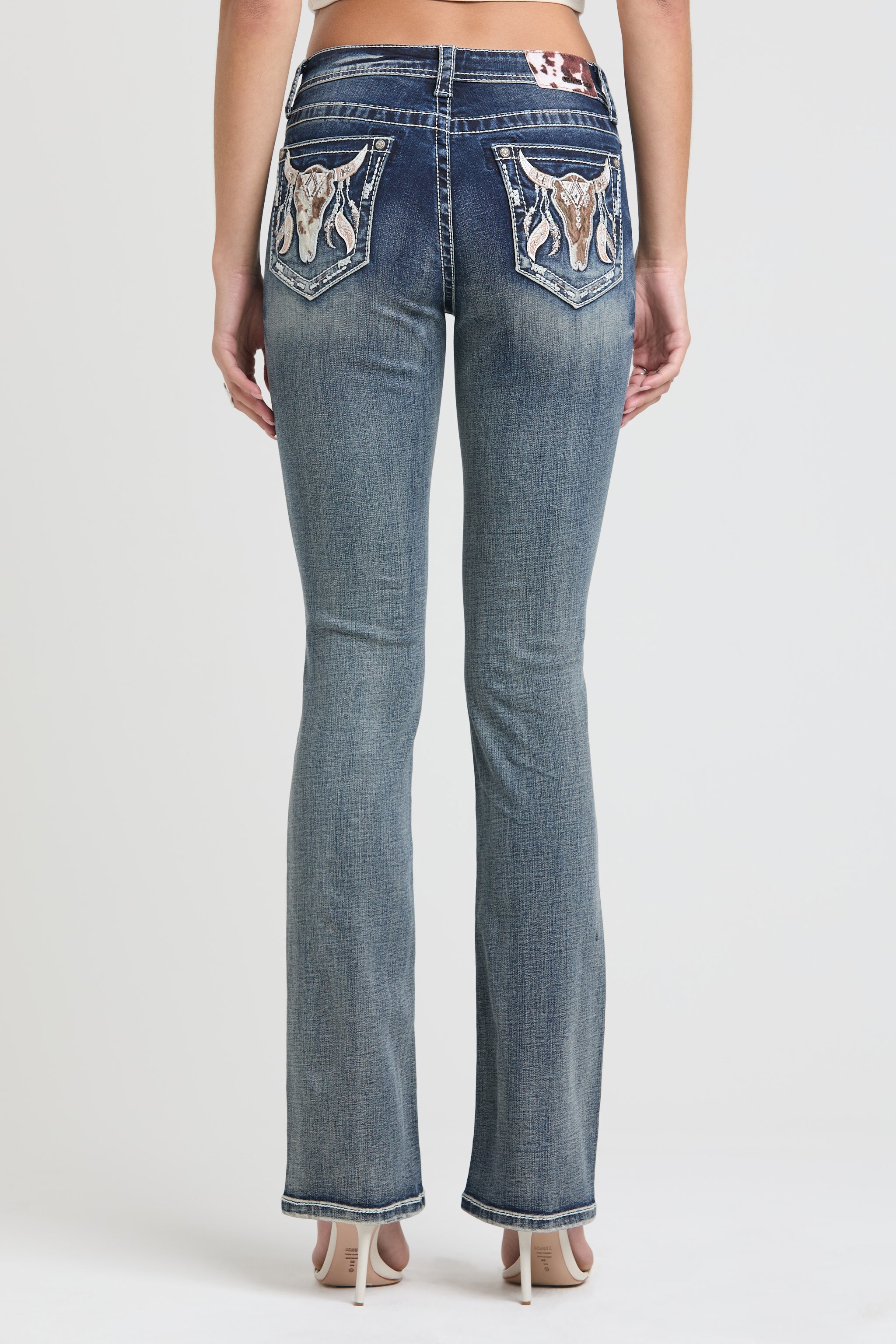 Grace in LA Women's Western Bootcut Jeans - Full Back View of Medium Wash Denim with Dual Bull Skull and Feather Pocket Embroidery