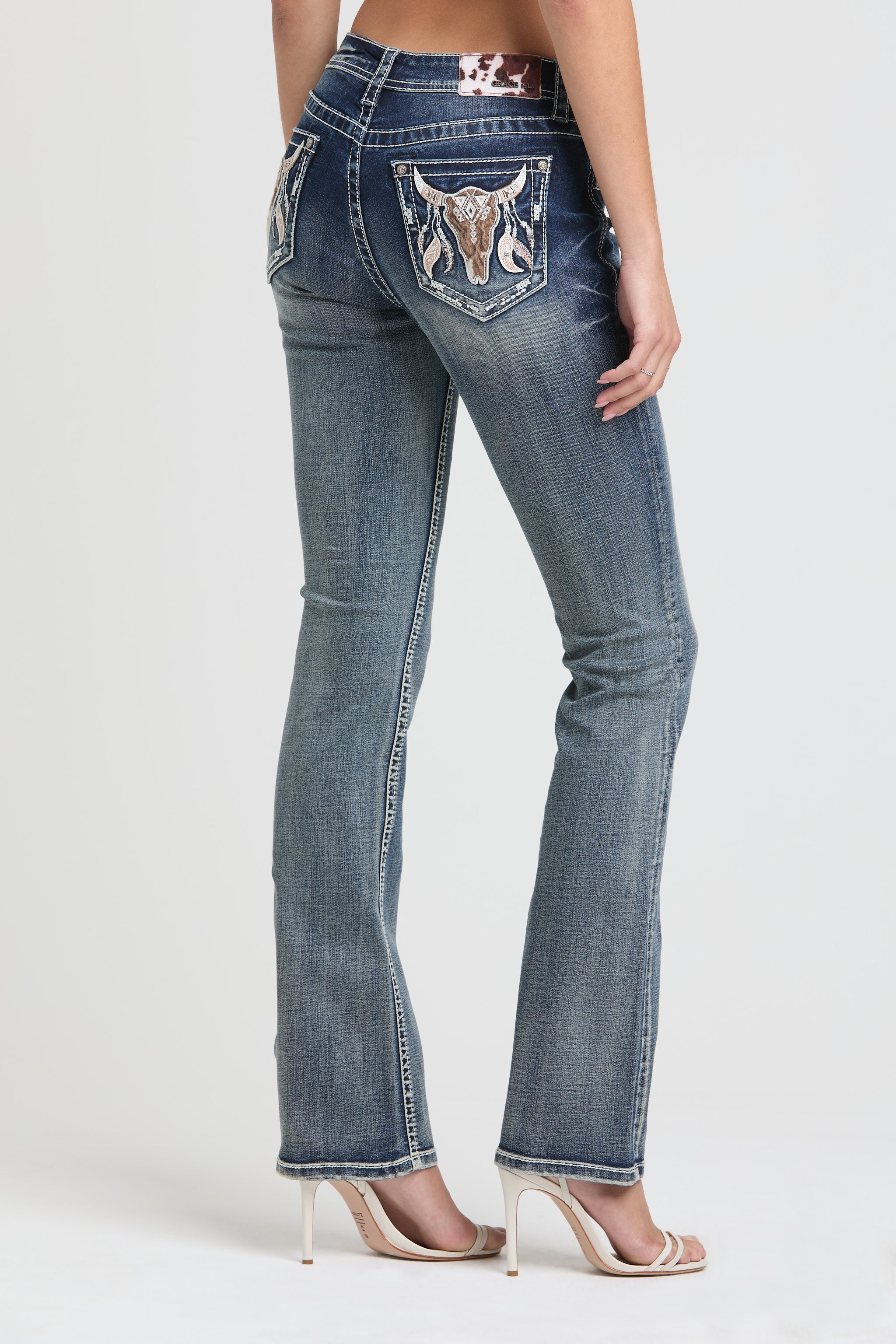 Grace in LA Women's Western Bootcut Jeans - Full Back View of Distressed Denim with Bull Skull and Feather Pocket Embroidery