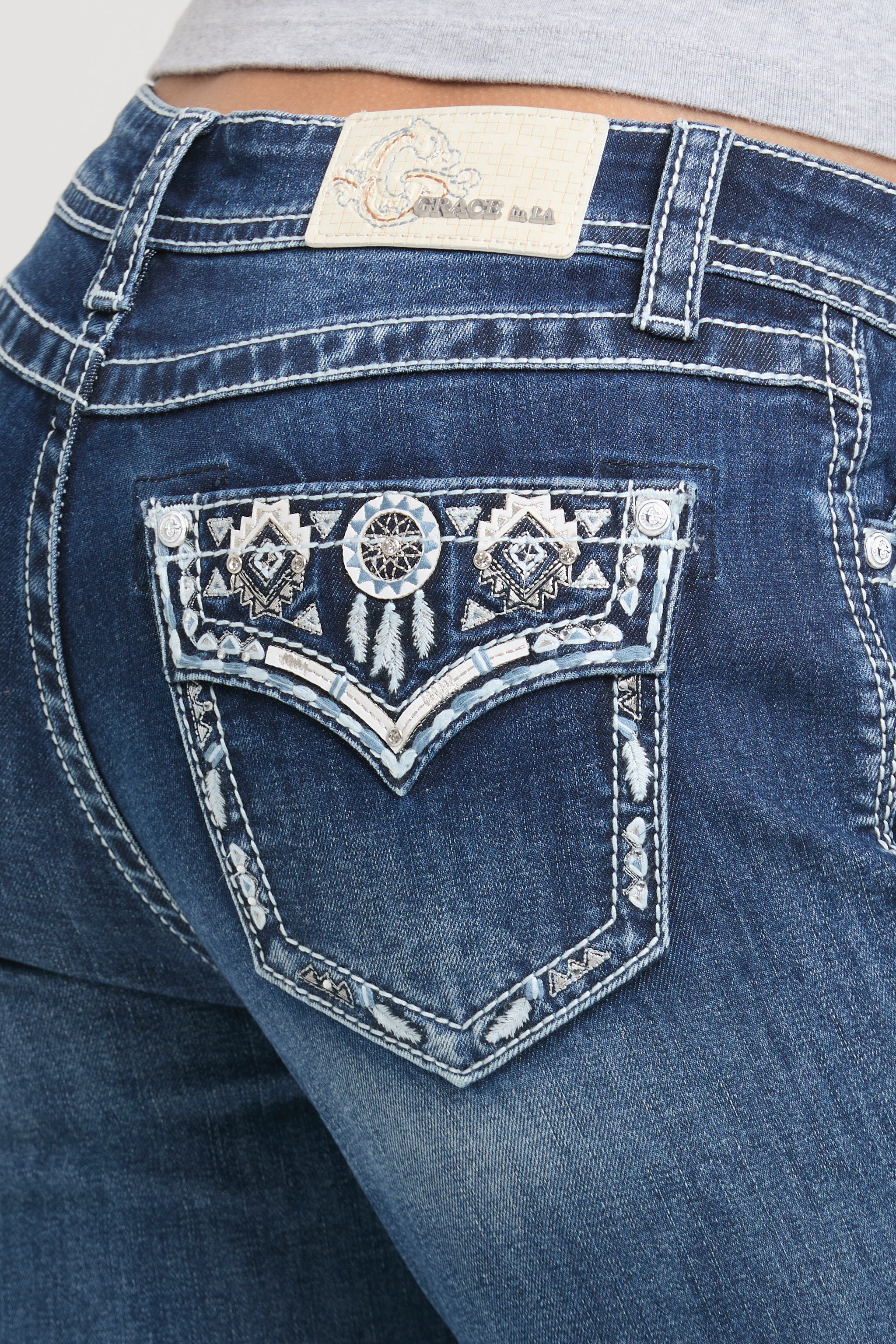 Grace in LA rhinestone jeans for women featuring a dark with a dreamcatcher and feather embroidery design on a pointed flap back pocket.