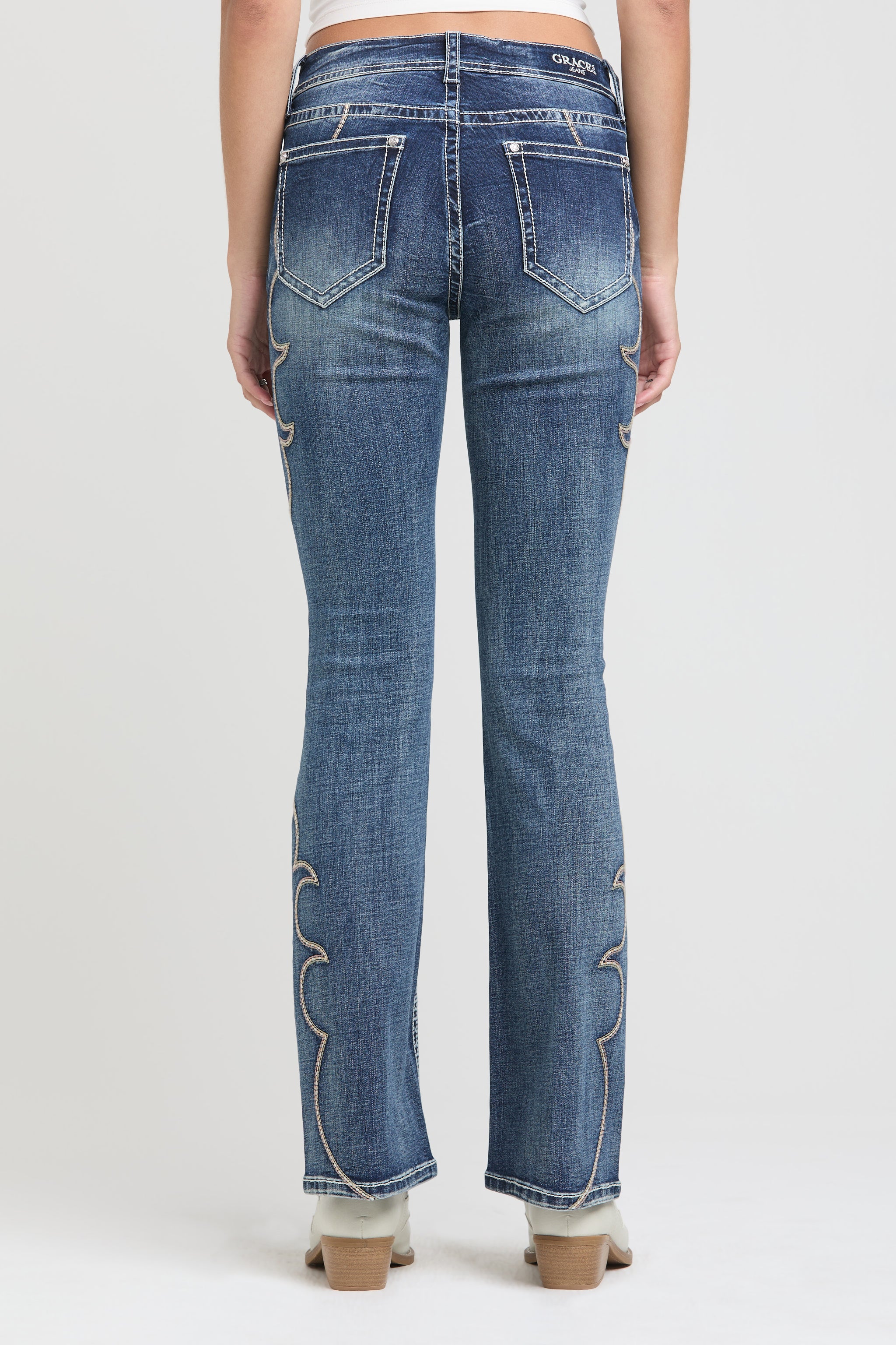 Grace in LA womens bootcut jeans in a dark featuring a full rear view with white contrast stitching and western-inspired scroll embroidery along the outer leg seams.