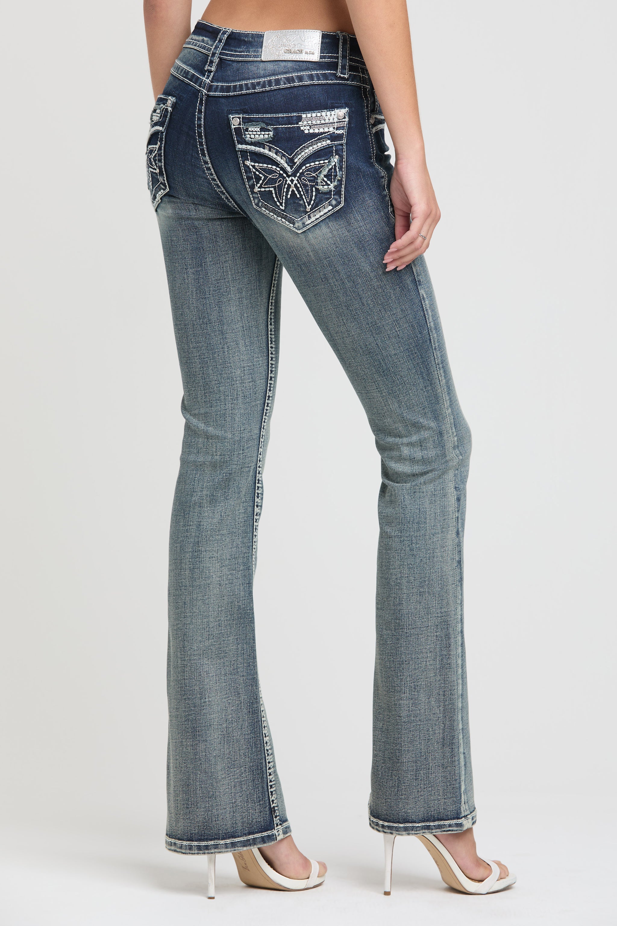 Grace in LA women's acid wash jeans in a slim bootcut fit featuring metallic silver wing embroidery and crystal accents on the back pockets.
