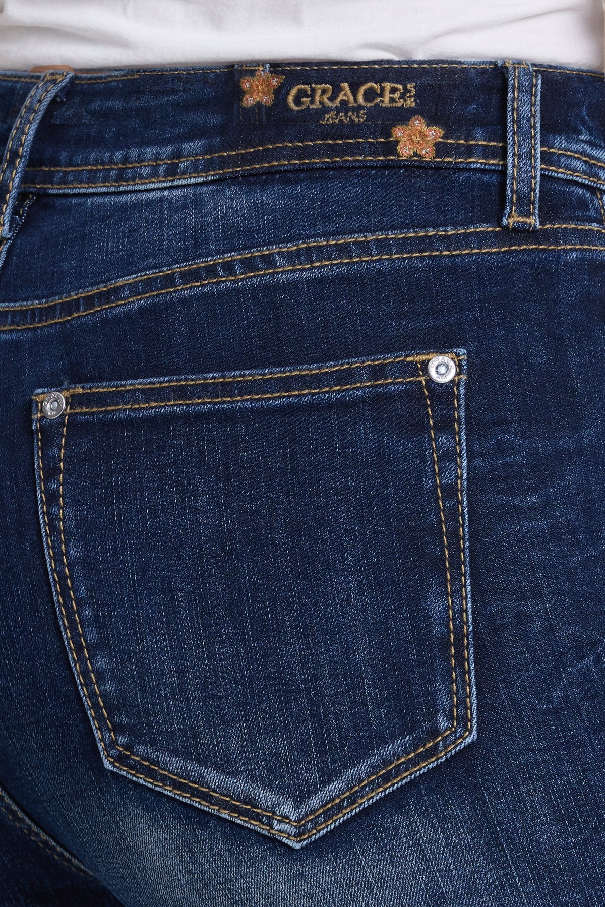 Close-up of the back waistband and pocket of dark blue denim jeans, showing the Grace in LA Jeans brand label and contrast stitching.