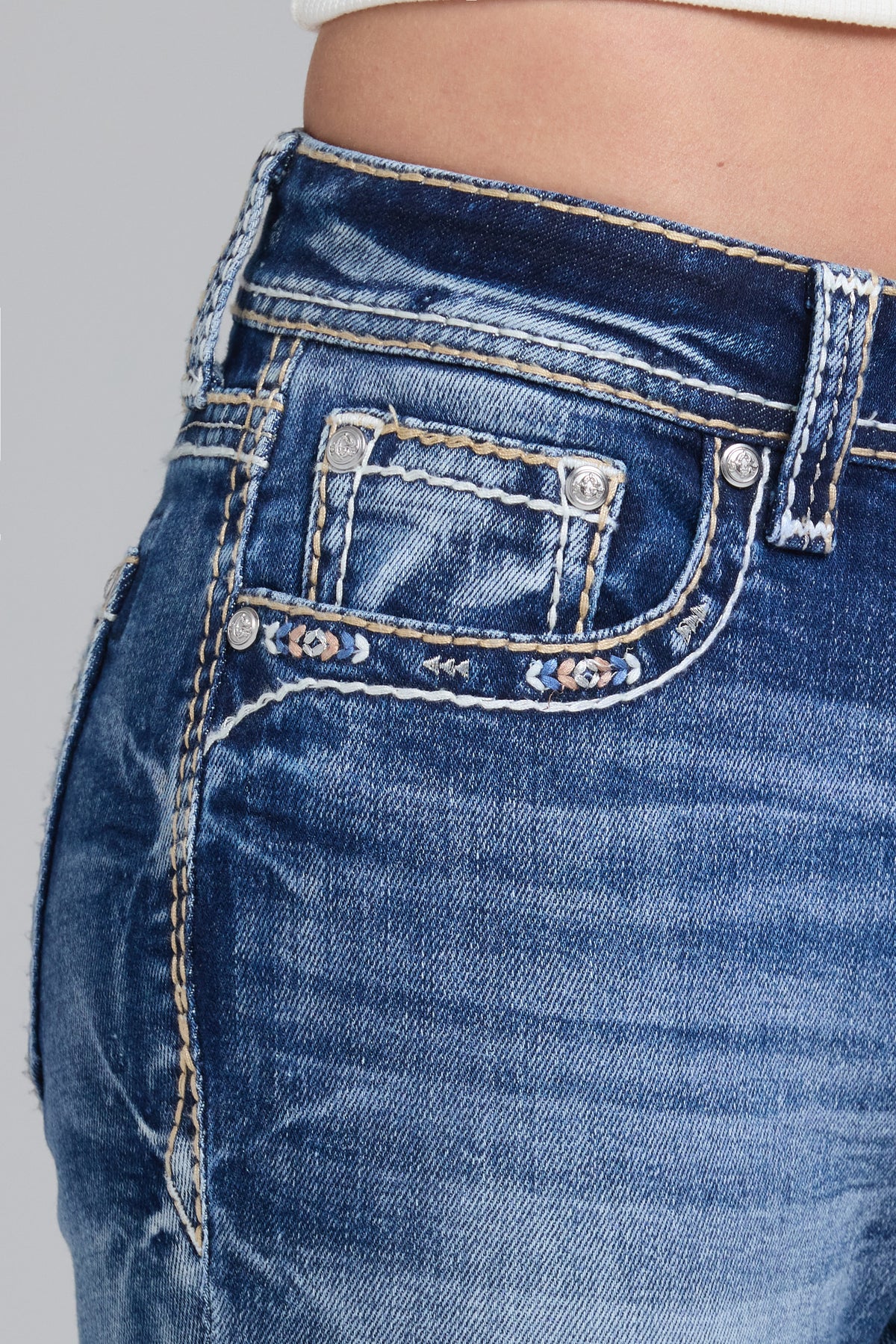 Close-up of a person wearing blue denim jeans, showing the back pocket, silver rivets, contrast stitching, and waistband details.