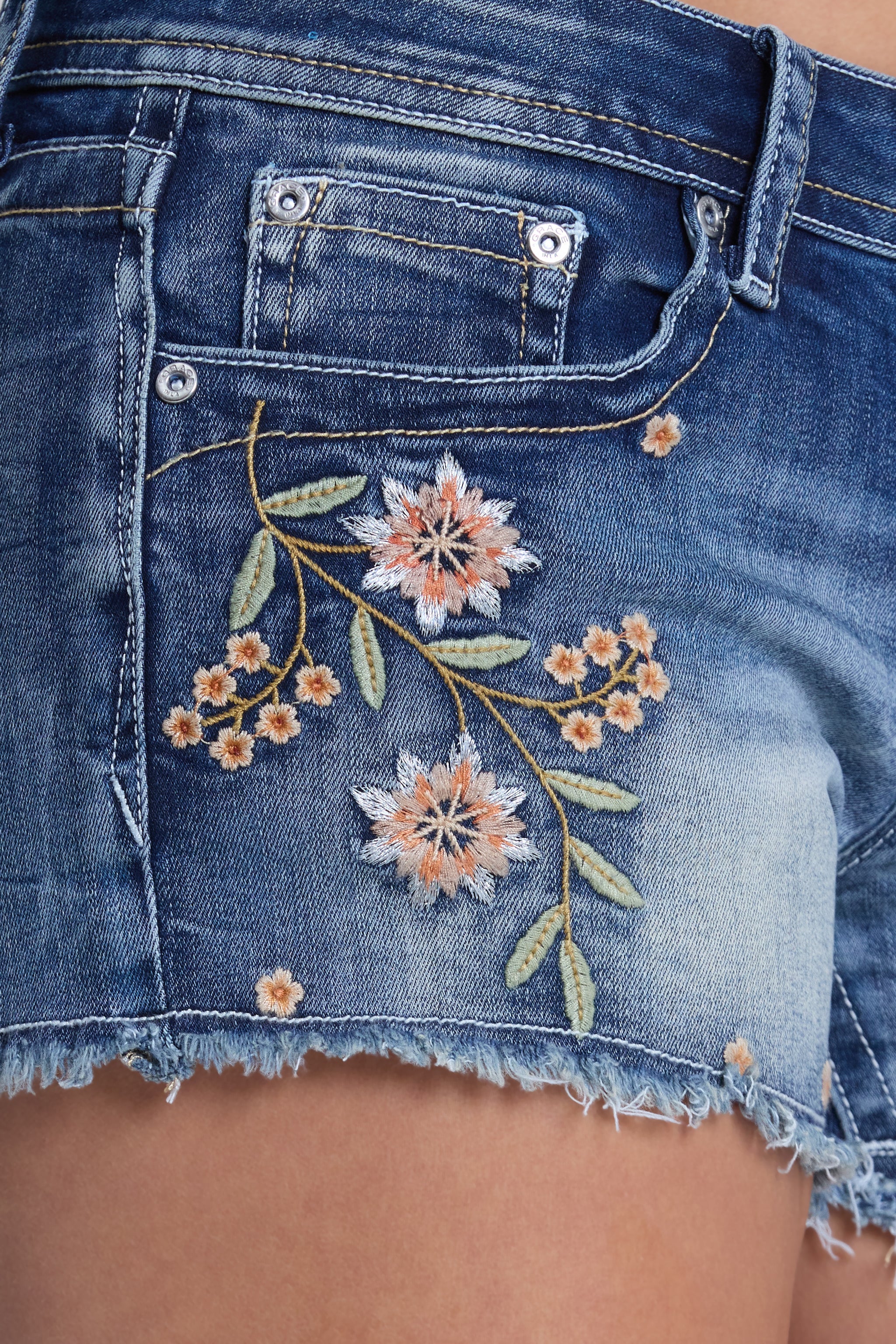 Grace in LA women's medium wash low-rise denim shorts featuring floral embroidery detailing on soft stretch denim