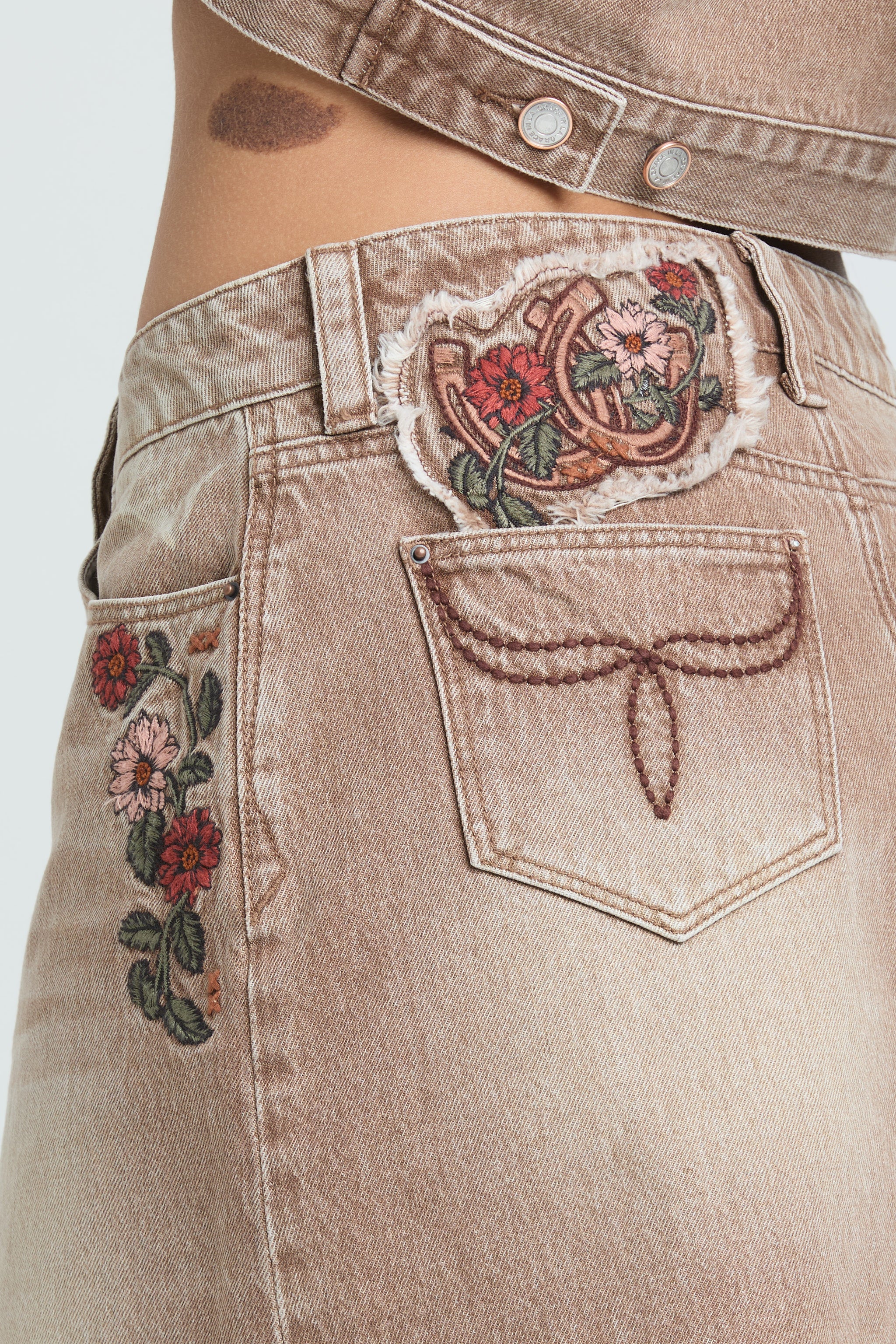 Grace in LA beige denim shorts with floral rose embroidery and a horseshoe-themed decorative back pocket patch.