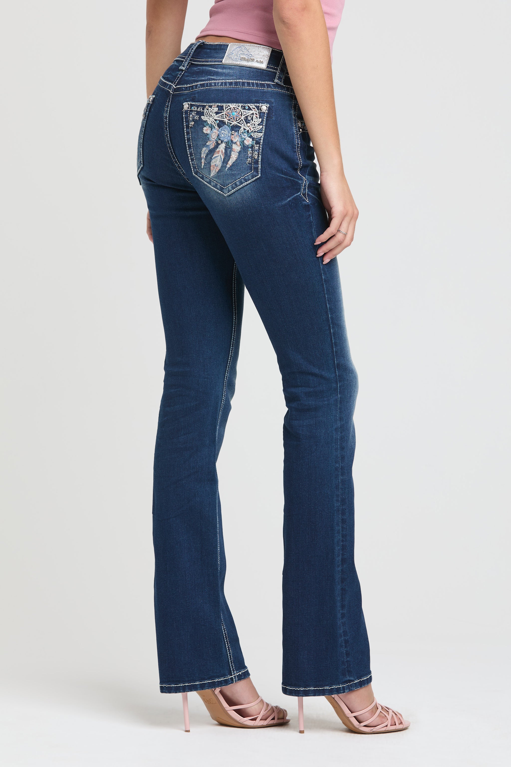 Grace in LA embroidered jeans women featuring an ornate western dreamcatcher motif on the back pocket with a large blue rose and colorful feather embroidery.