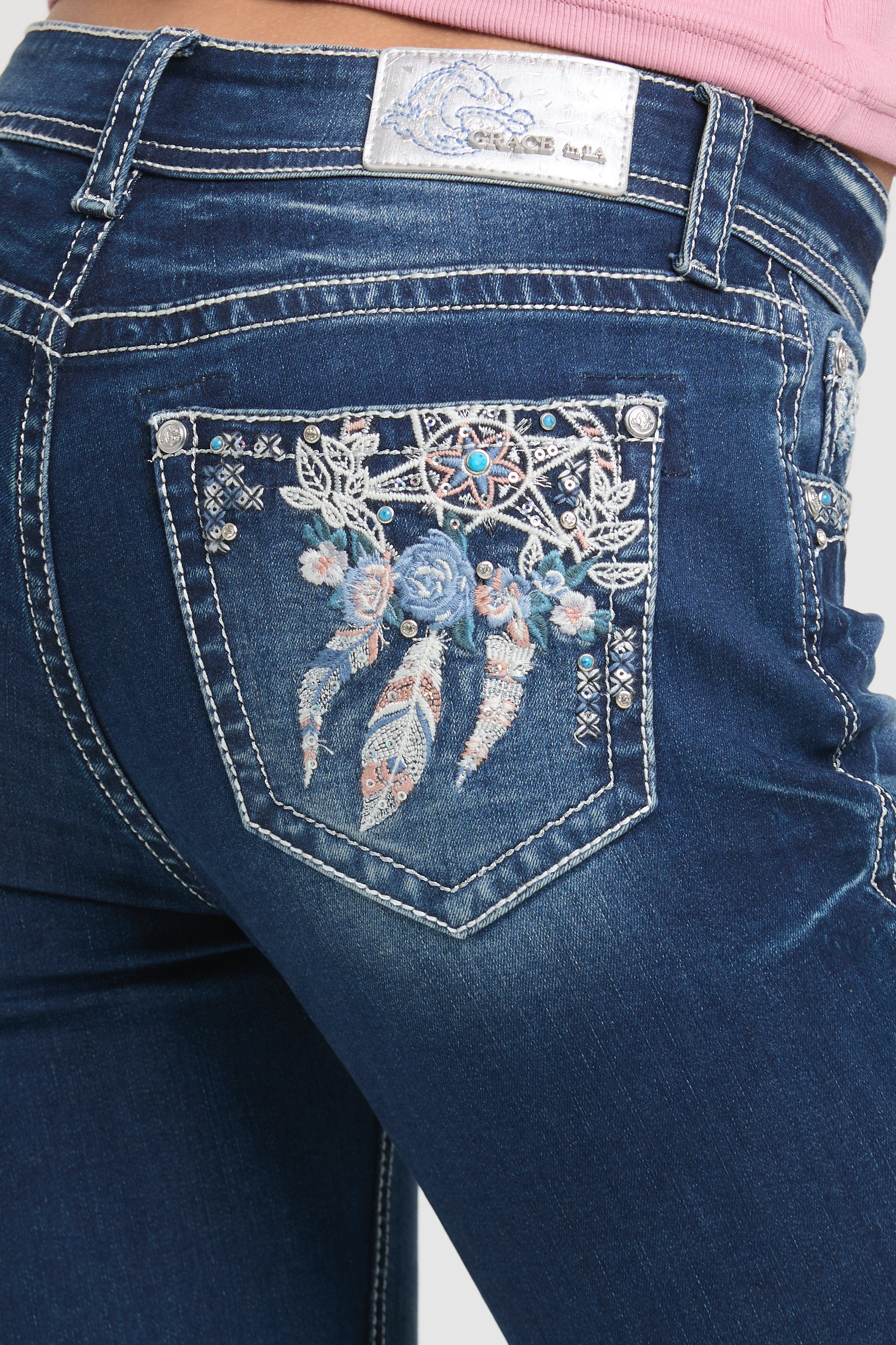 Grace in LA embroidered jeans women in a dark wash flare fit featuring an ornate western dreamcatcher and blue rose design on the back pockets.