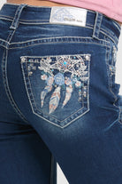 Grace in LA embroidered jeans women in a dark wash flare fit featuring an ornate western dreamcatcher and blue rose design on the back pockets.