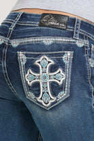 Grace in LA womens bootcut jeans featuring a back pocket with an ornate white embroidered cross design, turquoise crystal accents, and silver studs.
