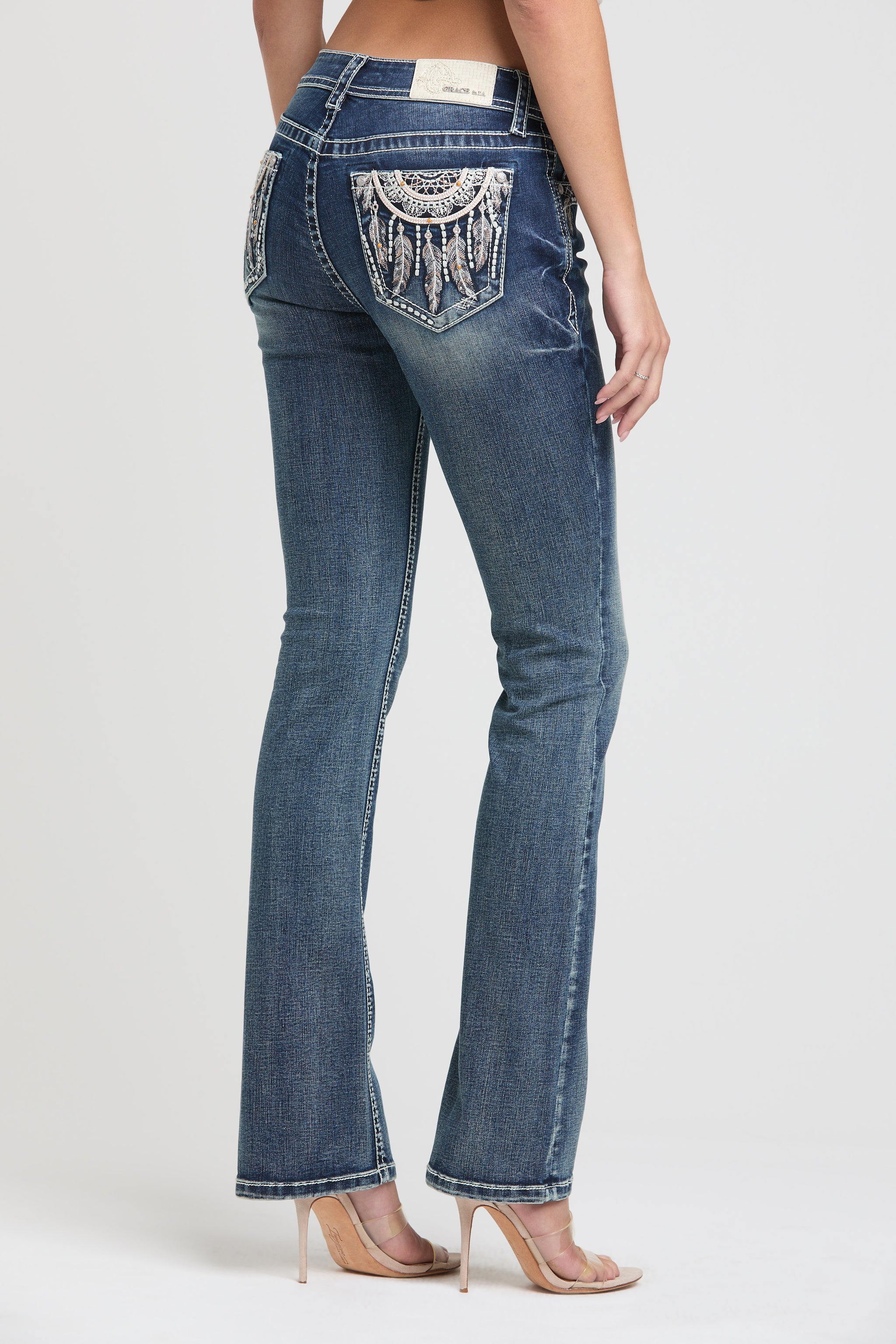 Grace in LA embroidered jeans women featuring a western horseshoe motif on the back pocket with intricate tribal star patterns and metallic silver stitching.