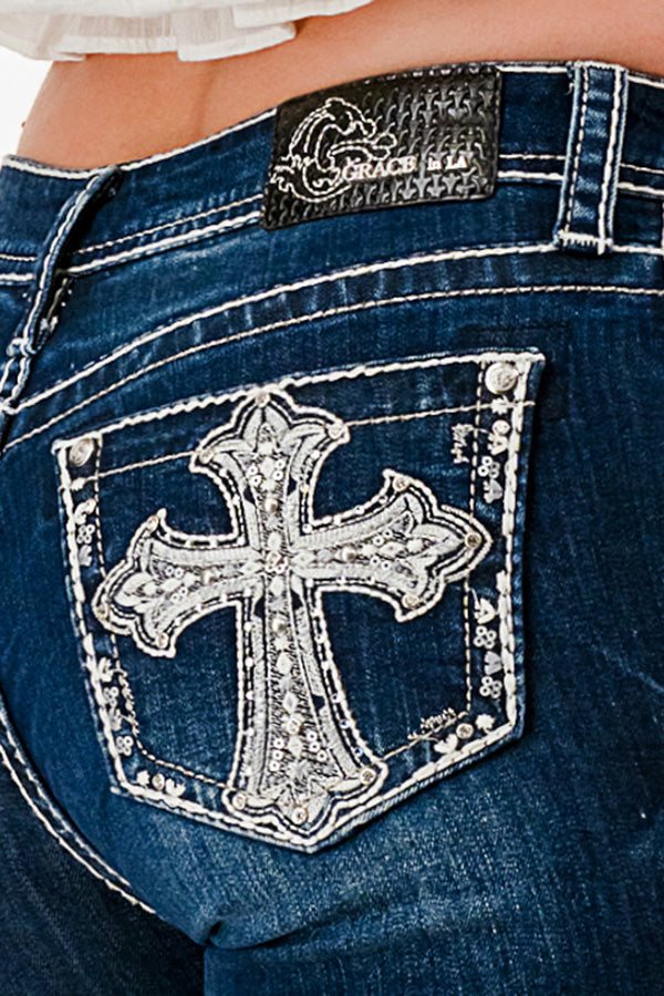 Grace in LA western jeans for women featuring a large silver rhinestone cross patch and intricate embroidery on the back pocket.