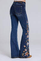 Blue jeans with a high-rise, flare silhouette, featuring detailed floral embroidery down the outer leg on the right side. The jeans are shown from a rear three-quarter angle on a model, set against a plain light gray studio background.