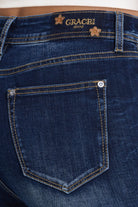 Close-up of the back waistband and pocket of dark blue denim jeans, showing the Grace in LA Jeans logo patch and contrast stitching.