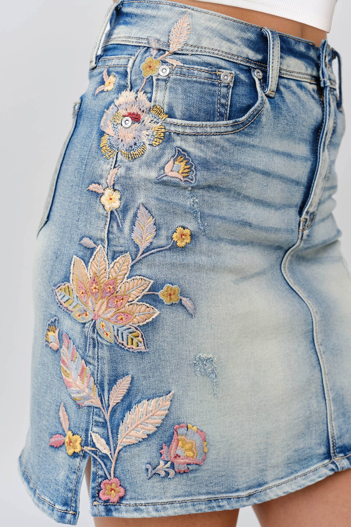 Grace in LA denim skirt close-up of floral colored embroidery on light wash denim